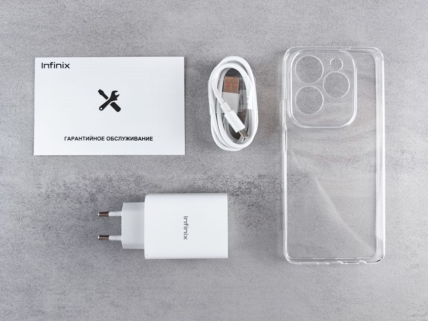 A flat lay of a transparent smartphone case with four camera cutouts, a white Infinix-branded charging brick, a white USB charging cable, a warranty card with a wrench icon and Russian text, all arran