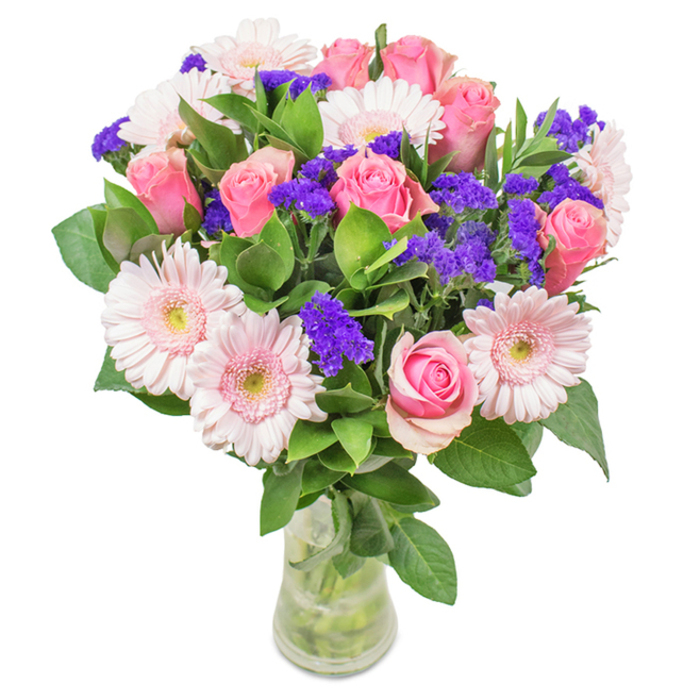 Set against a clean, white background, this eye-catching bouquet from North Ockendon boasts an expertly balanced palette of approximately seven to nine soft-to-medium pink roses, some with petals gently unfurling in classic spirals and others held in tight buds, suggesting new beginnings. Five to seven pale pink gerbera daisies, with large daisy-like heads and nearly white centres, bring youthful exuberance and generous fullness to the composition. Vivid purple clusters of statice wind gracefully between the larger blooms, their crisp texture and lively hue injecting a sense of movement and joyful depth. Lush, dark green leaves weave throughout, elevating the overall vibrancy and enhancing the bouquet's feeling of abundance-much like the flourishing hedgerows around town. Every stem is visible inside the transparent glass vase, rooted in clear water that suggests freshly cut botanicals straight from the grower. The bouquet makes a versatile North Ockendon gift, well-suited for birthdays, Mother's Day, office celebrations, or simply to fill a loved one's living space with joy and affection. Its artful structure, attention to nuance, and fresh, radiant colours are a testament to the dedication and skill found at Flowers North Ockendon.